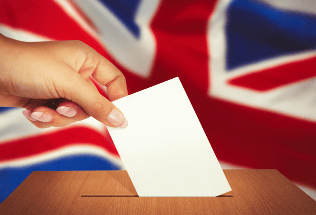 A person entering their slip into a ballot box with the Union Jack behind them.